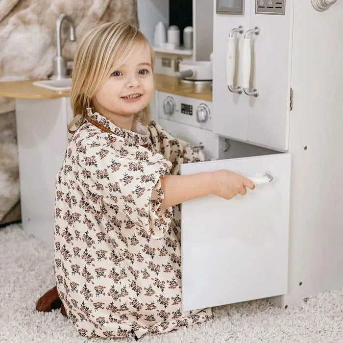 Smiling child playing with white wooden kids kitchen playset on carpet