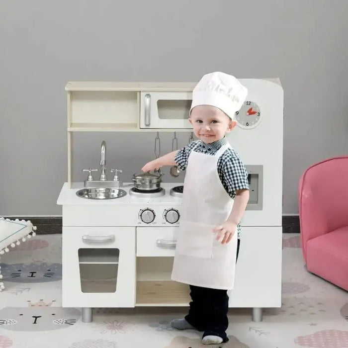 Child dressed as chef playing with white wooden toy kitchen set and stainless steel accessories