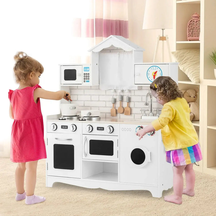 Two toddlers playing with a white wooden pretend kitchen set with stove, oven, microwave, sink, and utensils