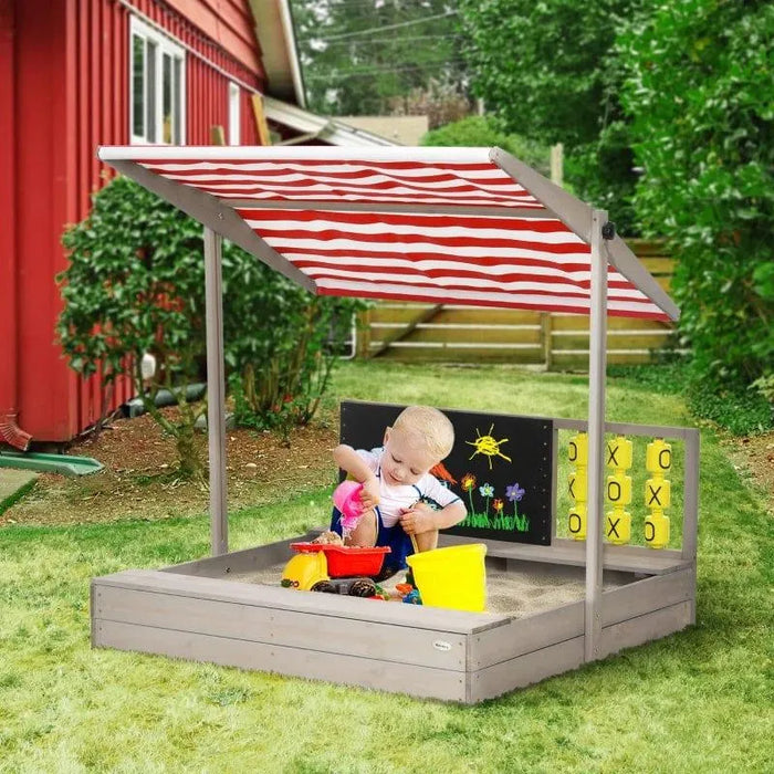 Child playing in grey wooden sandbox with canopy, board games, and chalkboard outdoors