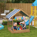 Kids playing in wooden sandbox with canopy and play accessories in a garden