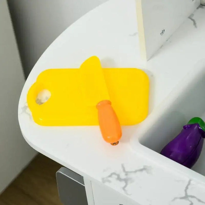 Kids wooden play kitchen with yellow toy knife and board on white countertop, toy eggplant in sink