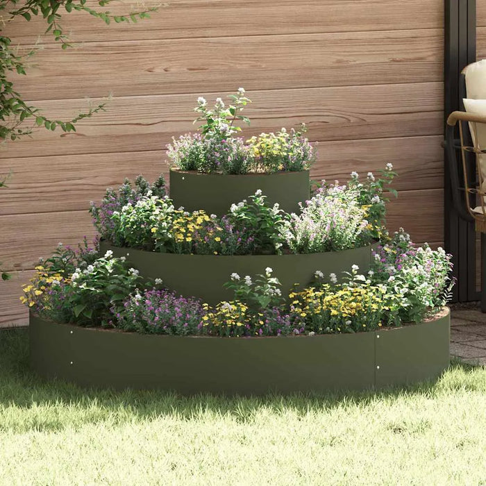 Three-tiered olive green cylindrical metal planter with mixed colorful flowers on grass against wooden fence