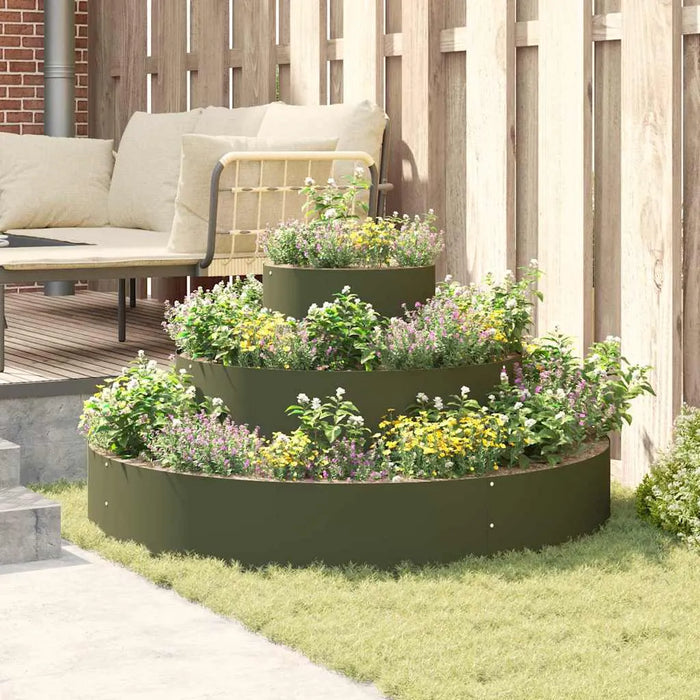 Three-tier olive green cylindrical steel planter with flowers in a cozy backyard seating area