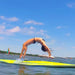 Woman in bikini doing backbend on large yellow foam water float in lake with boats