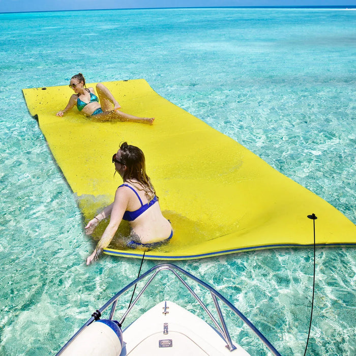 Two women relaxing on a large yellow foam water float in clear blue ocean by a boat