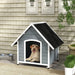 Large grey and black wooden dog kennel with slanted roof, yellow lab inside, outdoor patio