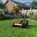 Red lawn mower on a green lawn with a house and garden in the background