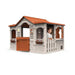 French-inspired playhouse with orange roof, white walls, and a smiling child at the window