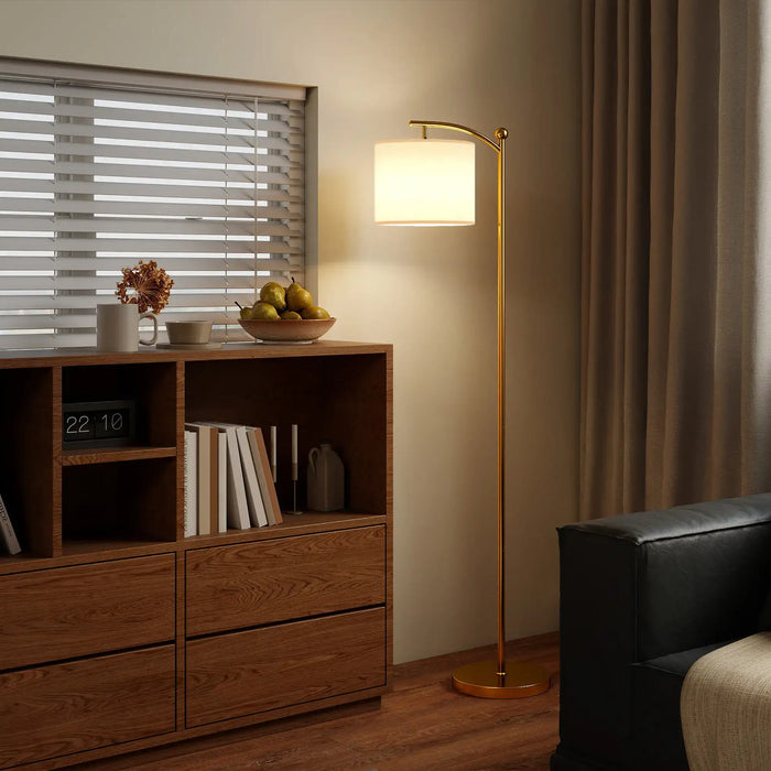 Modern gold LED floor lamp with cream shade next to wooden shelf and black sofa in cozy living room