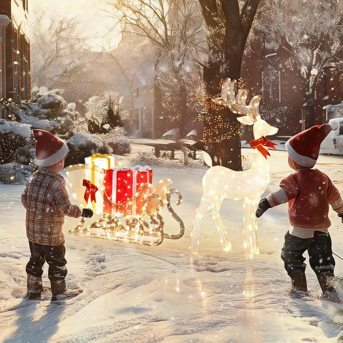 Two children in winter clothing playing with a reindeer and sleigh decoration in a snowy outdoor setting.