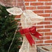 Decorative deer figure with a red bow against a brick wall and Christmas tree background