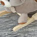 Grey plush rocking horse bear on wood base, striped rug background, soft toy design