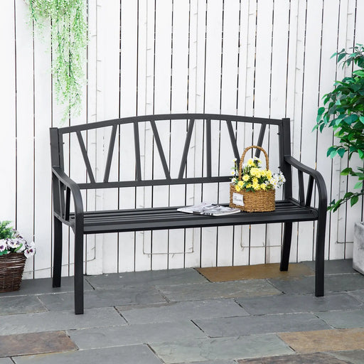 Black metal outdoor garden bench with high back and armrests, decorated with wicker basket of yellow and white flowers, set against white wooden fence