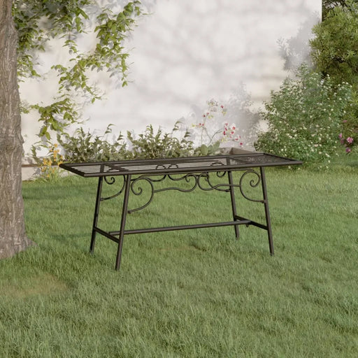 Black metal outdoor bench with scrollwork design on grass near tree and garden flowers