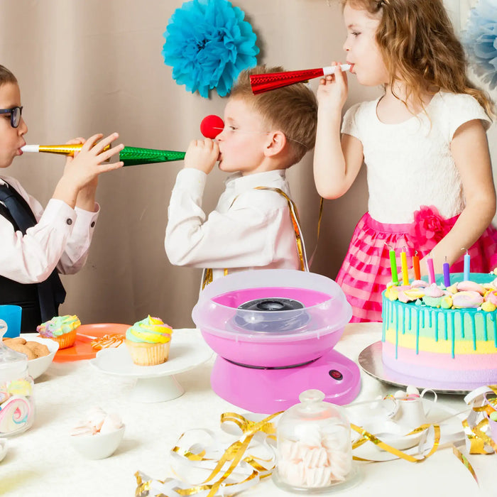 Children blowing party horns at a birthday party with a cake and cotton candy machine.