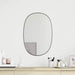 Round mirror on a white wall above a wooden shelf with decorative items.