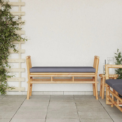 Modern bamboo garden bench with grey cushion on patio against white wall with greenery