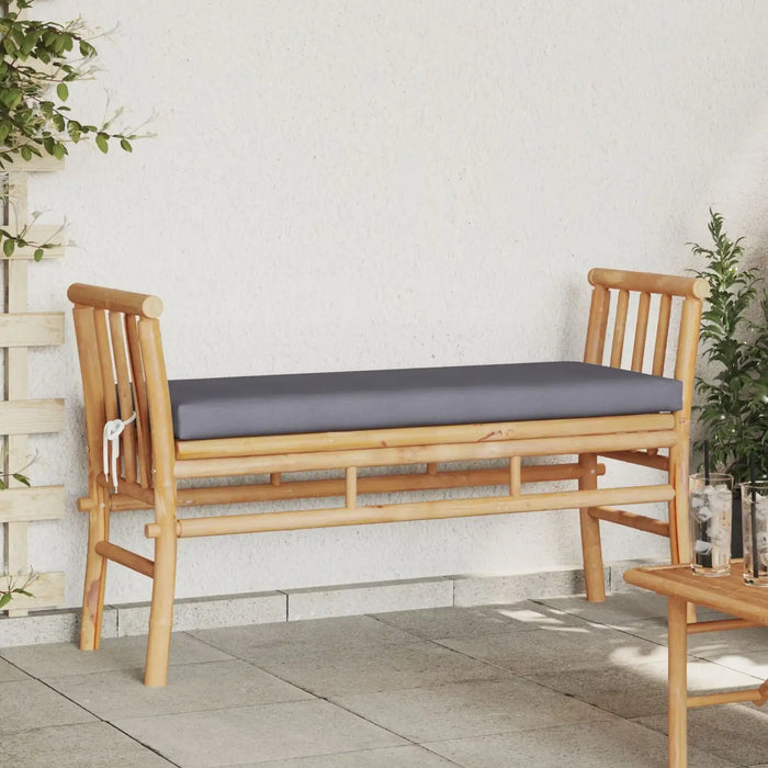 Modern bamboo garden bench with grey cushion on patio, surrounded by plants and table with drinks