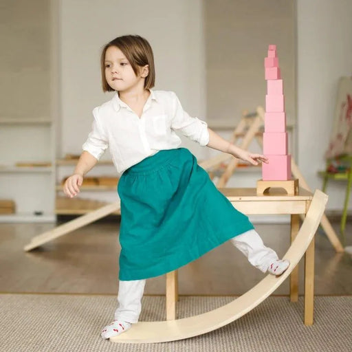 Child balancing on natural beech wood wobble board with ropes in bright indoor playroom