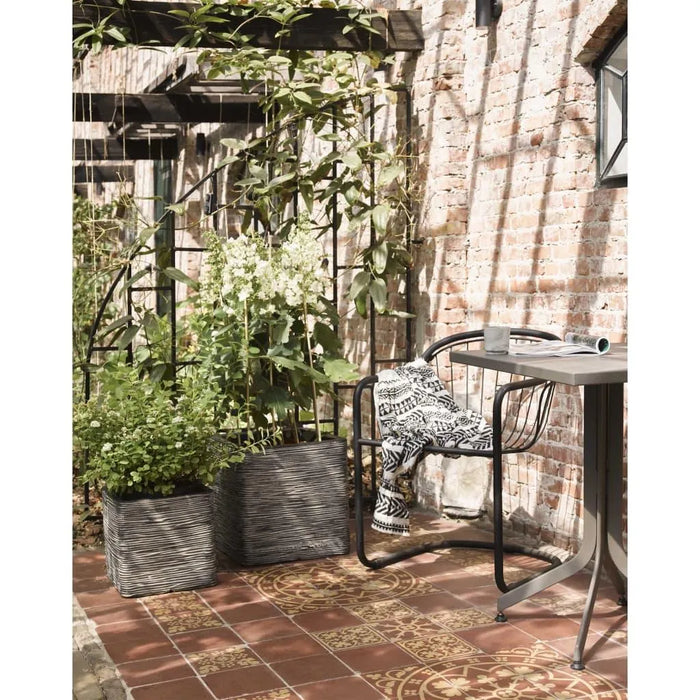 Anthracite ribbed flower pots with greenery on a tiled patio beside a brick wall seating area