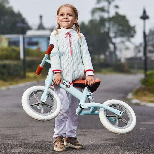 Smiling child outdoors holding blue no-pedal balance bike with adjustable seat and metal frame