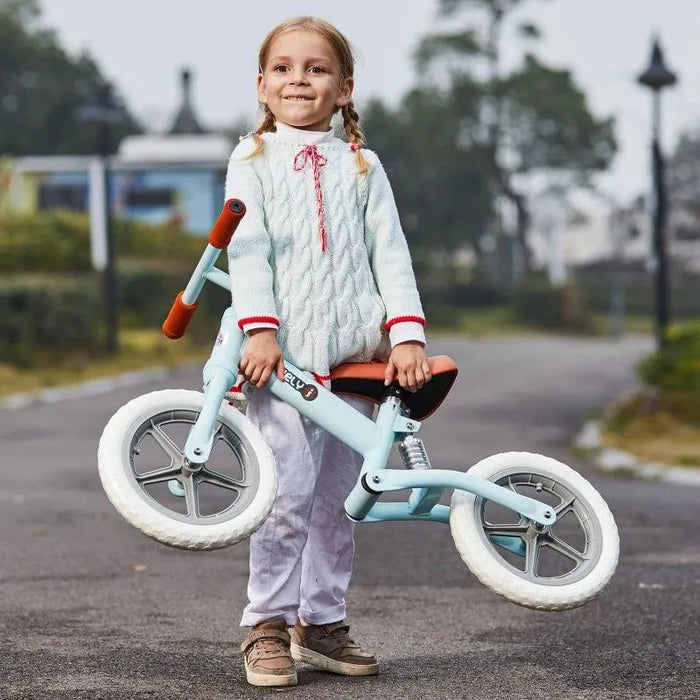 Smiling child outdoors holding blue no-pedal balance bike with adjustable seat and metal frame