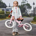 Smiling girl holding pink no-pedal balance bike with adjustable seat outdoors
