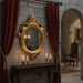 Decorative interior with a gold mirror, candles, and red curtains in a stone-walled room.
