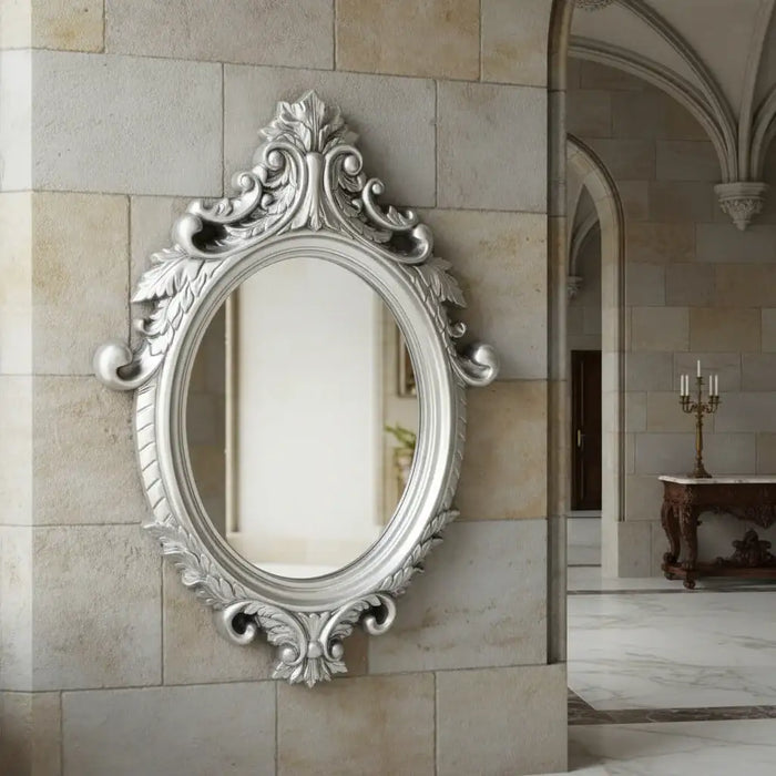 Decorative silver mirror with intricate designs on a stone wall.
