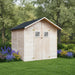 Light wood garden shed with black roof and double doors surrounded by green grass and colorful flowers