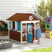 Child playing in outdoor wooden garden playhouse with blue door and flower boxes
