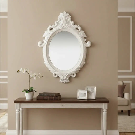 Decorative white mirror on a beige wall above a wooden console table with a plant and framed photos.