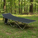 Black portable military folding camping cot with steel frame and side pocket in a forest