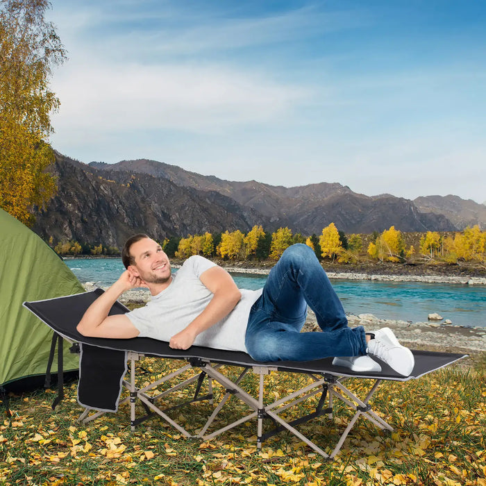 Man relaxing on a black folding camping cot with steel frame by a tent near river and mountains