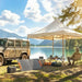 Outdoor camping scene by lake with beige tent, portable solar panels, off-road vehicle, and person fishing