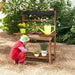 Child playing at wooden kids potting bench table with plants and yellow watering can outdoors
