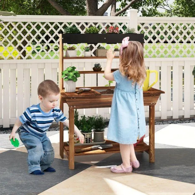 Kids playing at a wooden pretend play potting bench table with plants outdoors