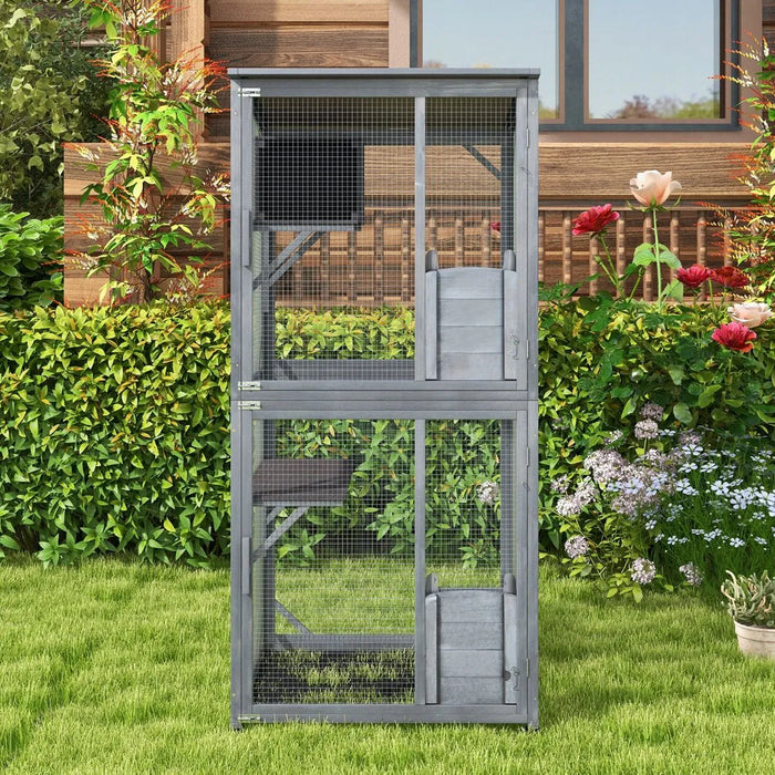 Two-level gray outdoor wooden rabbit hutch with wire mesh doors in garden with flowers and green grass