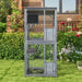 Two-level gray outdoor wooden rabbit hutch with wire mesh doors in garden with flowers and green grass