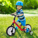 Toddler boy wearing blue helmet and striped shirt riding red balance bike on green grass
