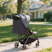 Gray stroller on a sidewalk with a house and trees in the background