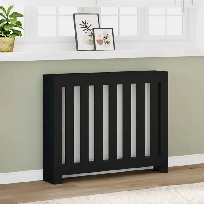 Black radiator cover with decorative slats in a room with a white shelf, plant, and framed pictures.