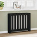 Black radiator cover with decorative slats in a room with a white shelf, plant, and framed pictures.