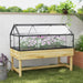 Raised wooden garden bed with transparent polycarbonate cold frame roof and blooming white and pink flowers
