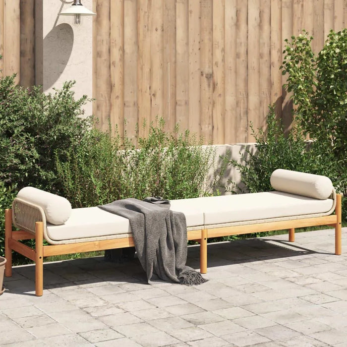 Rattan garden bench with cream cushion on patio, wooden fence and greenery behind