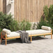 Rattan garden bench with cream cushion on patio, wooden fence and greenery behind