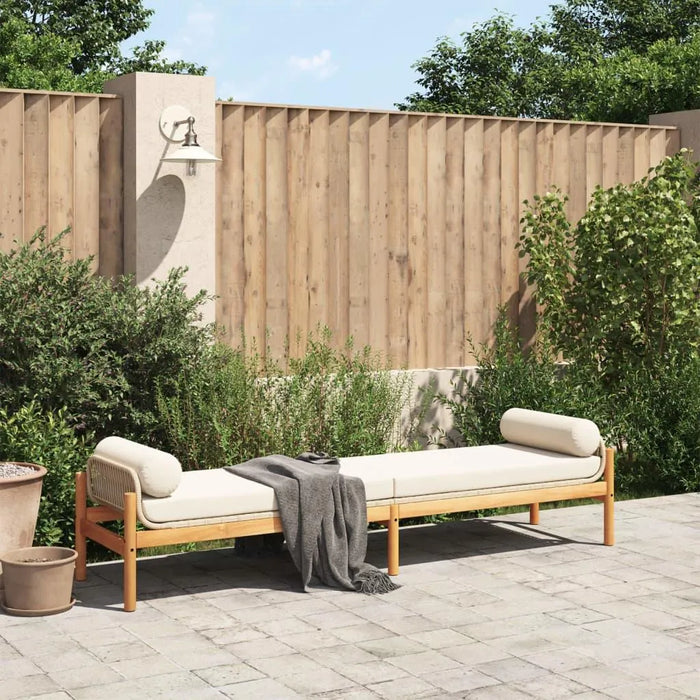 Rattan garden bench with cream white cushion on patio, wooden fence and greenery background