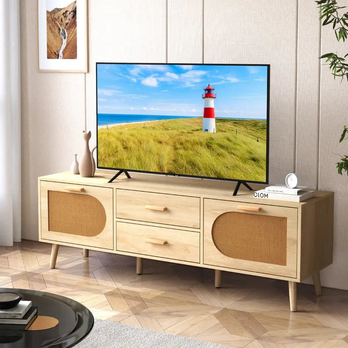 Natural wood TV stand with rattan cabinet doors and drawers, supporting a 65-inch flat screen displaying a lighthouse.