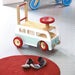 Retro wooden campervan walker and ride-on toy with red wheels on a playroom floor